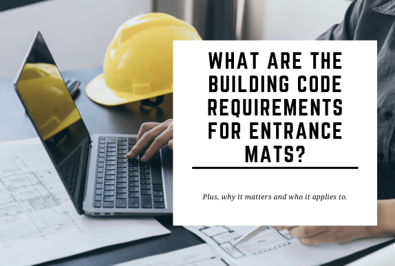 A yellow hard hat and a laptop are placed on a desk where someone is working. The blog header reads What are The Building Code Requirements for Entrance Mats?