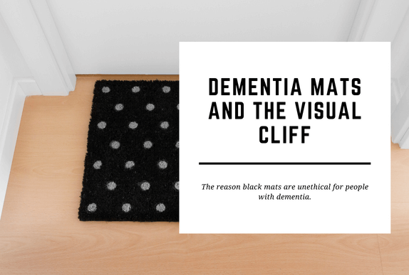 A dementia black mat sits in front of a closed white door. The blog header reads Dementia Mats and the Visual Cliff.