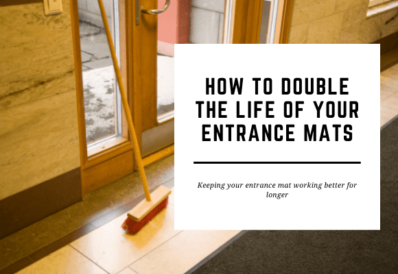 An entrance mat is laid inside a doorway with a broom leaning against the door. The blog header reads How to Double the Life of Your Entrance Mats.